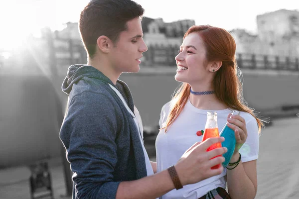 Young couple enjoying tasty cocktails and standing with glass bottles — Stock Photo, Image