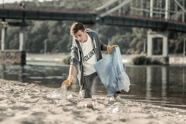 Молодой темноволосый волонтер проводит день, очищая песок на пляже. — стоковое фото