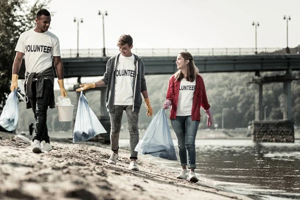 Tres voluntarios caminando cerca del río con bolsas de basura recogiendo basura — Foto de Stock