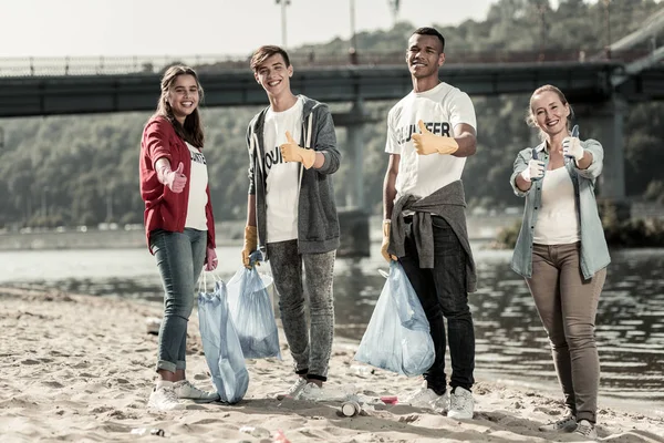 Bedrijf van jonge vrijwilligers verhogen hun duimen omhoog met hun teamleider — Stockfoto