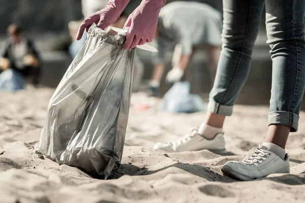 Крупный план молодого студента в джинсах и кроссовках, убирающего мусор на пляже — стоковое фото