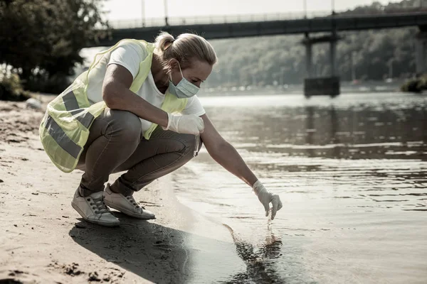 Trabajador del servicio de inspección sanitaria sentado cerca del río comprobando el agua — Foto de Stock
