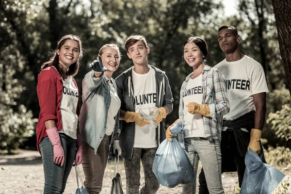 Jóvenes voluntarios activos sosteniendo bolsas de basura con basura después de limpiar el bosque — Foto de Stock