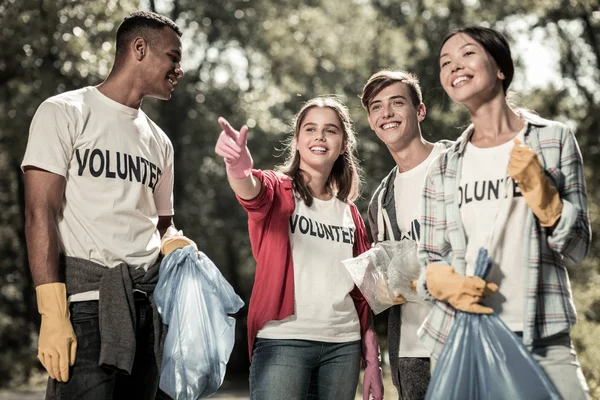 Улыбающиеся юные ученики чувствуют себя вовлеченными в уборку леса и волонтерство — стоковое фото