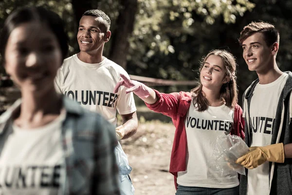Dark-haired meisje permanent met haar vrienden tijdens het vrijwilligerswerk in bos — Stockfoto