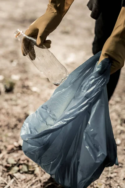 Hombre voluntario en el bosque usando guantes amarillos mientras recoge botellas vacías —  Fotos de Stock