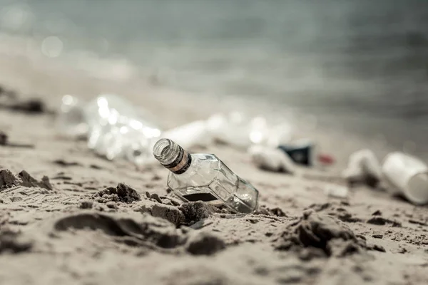 Закрыть пустую стеклянную бутылку спирта, лежащую на песке у реки — стоковое фото