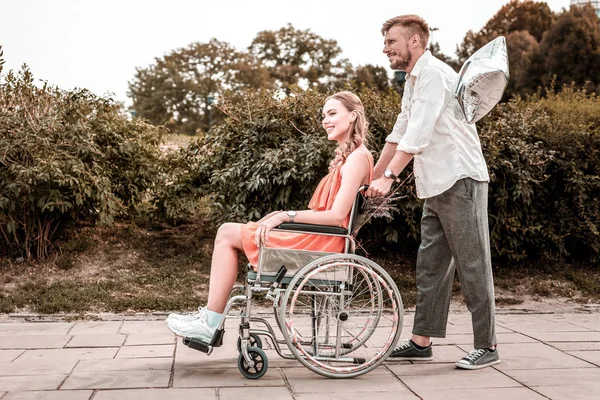 Glad flicka leende medan pojkvän driver hennes rullstol — Stockfoto