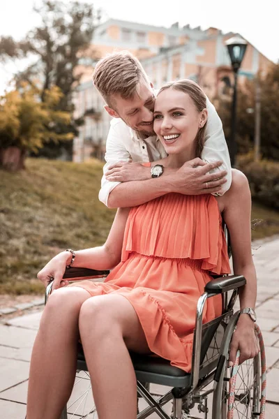 Happy girl sitting in wheelchair and caring boyfriend hugging her