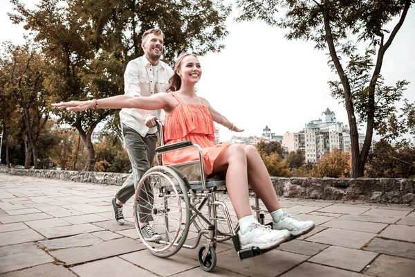 Chica feliz fingiendo estar volando mientras monta en su silla de ruedas — Foto de Stock