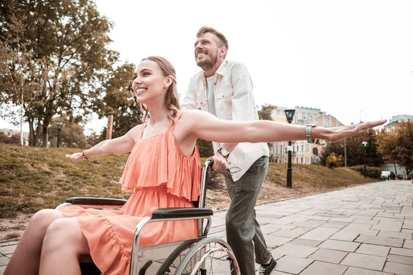 Девушка-инвалид с поднятыми руками и мужчина, толкающий ее инвалидное кресло — стоковое фото