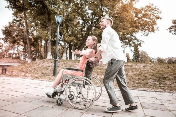 Άτομα με ειδικές ανάγκες κορίτσι απολαμβάνοντας βόλτα στο πάρκο και ο φίλος της, σπρώχνοντας το αναπηρικό αμαξίδιο — Φωτογραφία Αρχείου