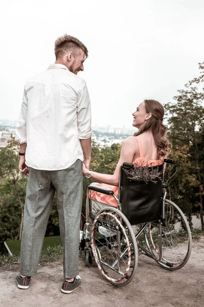 Jong meisje zittend in de rolstoel en het bedrijf van de hand van haar vriendje — Stockfoto