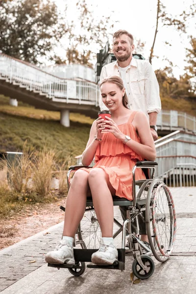 Ung man driver rullstolen och hans flickvän hålla glas kaffe — Stockfoto