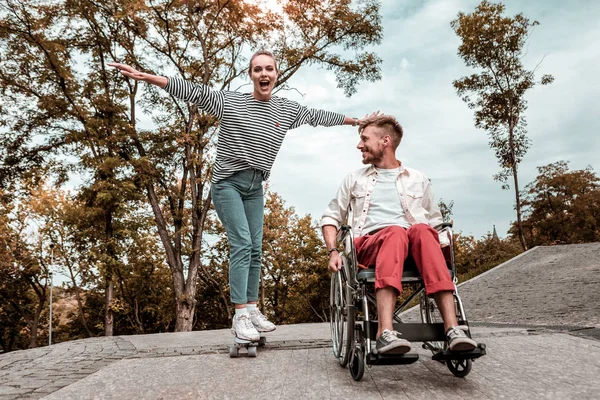 Emocional chica montando su monopatín mientras pasa tiempo con el hombre discapacitado — Foto de Stock