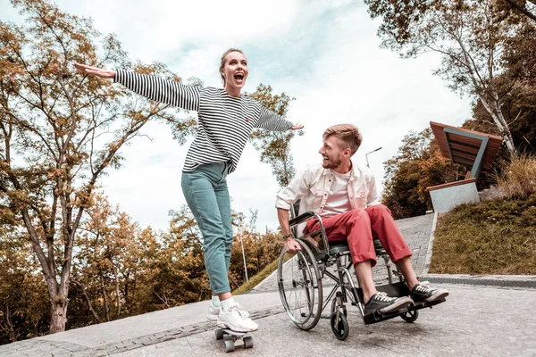 Glada kvinna stående på penny board och funktionshindrade man tittar på henne — Stockfoto
