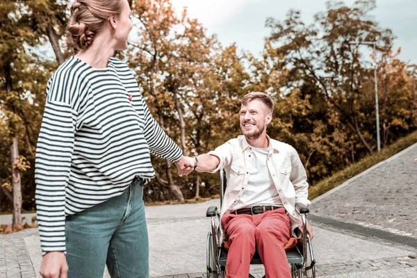 Hombre alegre mirando a su novia mientras está sentado en la silla de ruedas — Foto de Stock