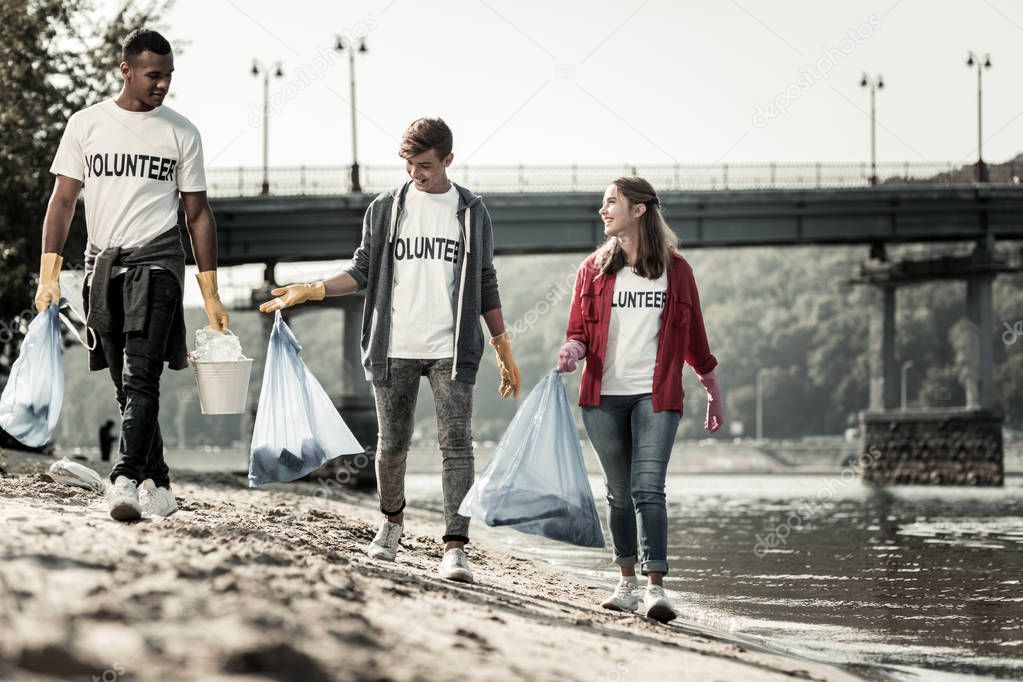 Three volunteers walking near the river with garbage bags gathering trash