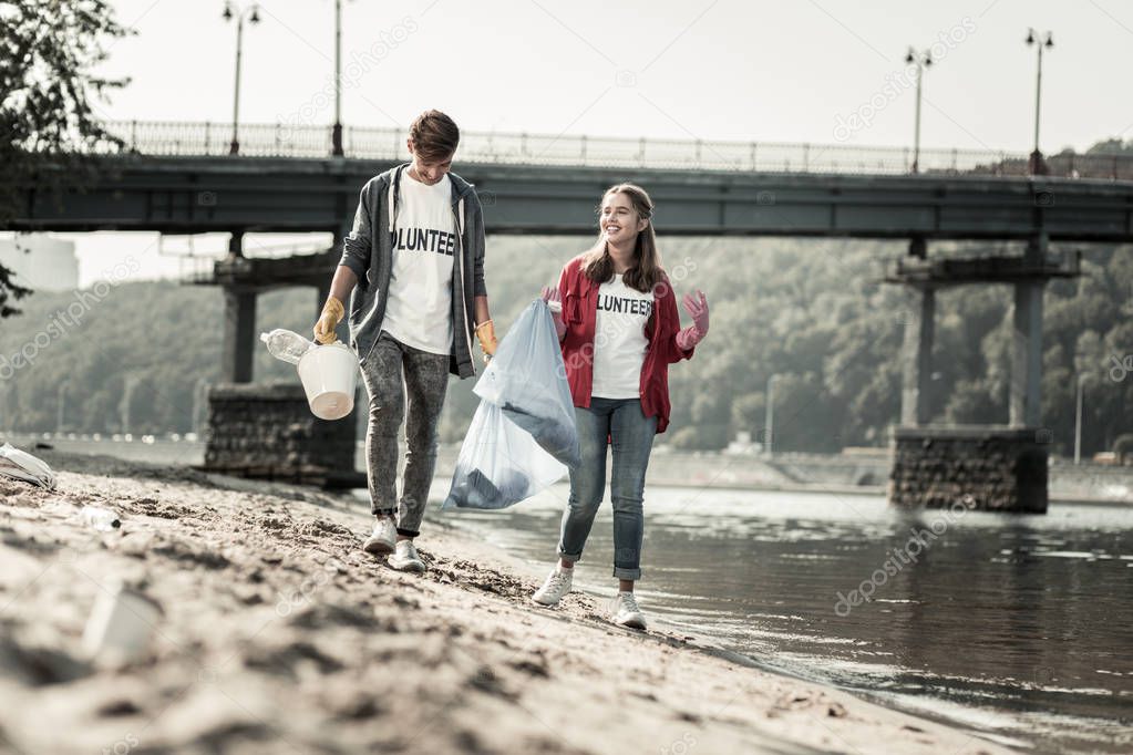 Beaming dark-haired girl feeling joyful while cleaning the beach with her brother