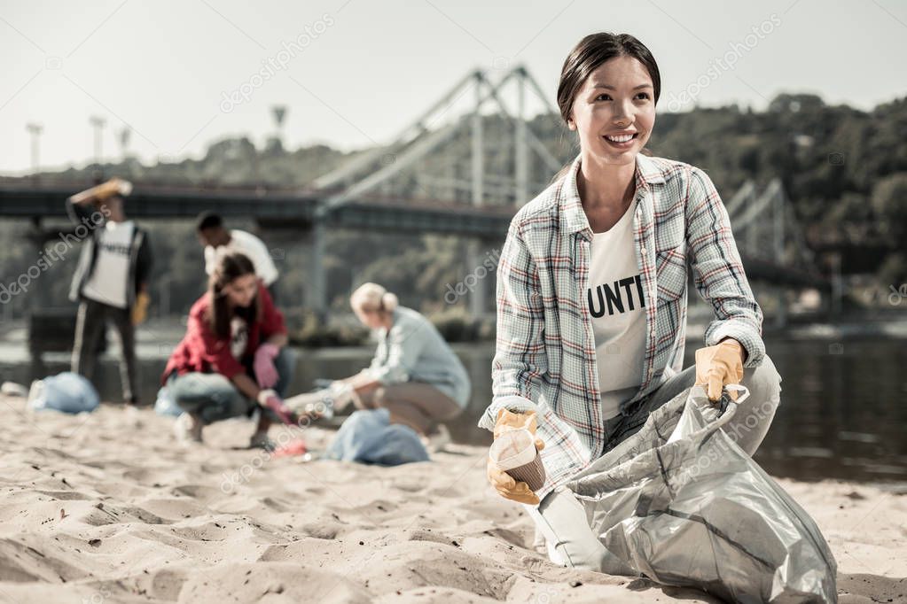 Beautiful dark-haired woman wearing squared shirt volunteering cleaning the beach