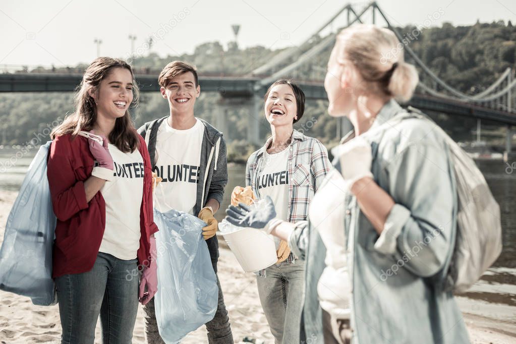 Three beaming students laughing while talking to their teacher volunteering together