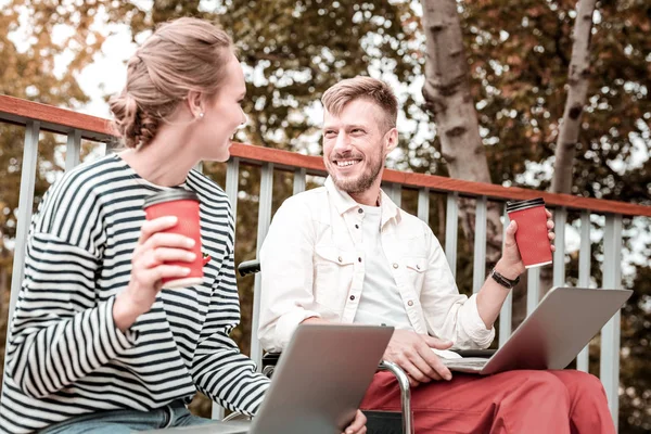 Amigos felices sosteniendo computadoras portátiles y tomando café en el parque — Foto de Stock