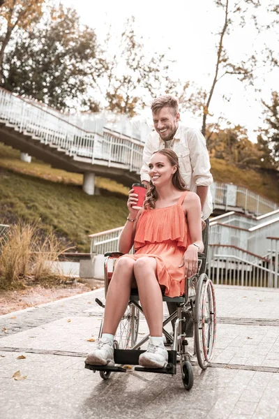 Девушка-инвалид наслаждается утренним кофе и ее парень толкает ее инвалидное кресло — стоковое фото