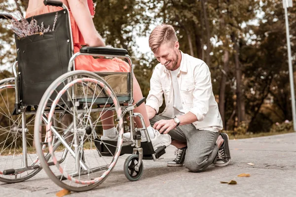 Молодой человек улыбается, завязывая шнурки девушке-инвалиду — стоковое фото