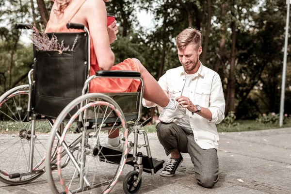 Hombre útil sonriendo y atando cuidadosamente los cordones de los zapatos de su novia — Foto de Stock