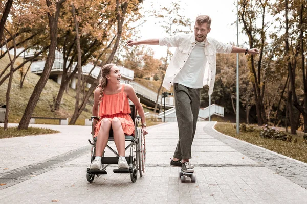 Excited man riding skateboard and disabled girlfriend smiling to him