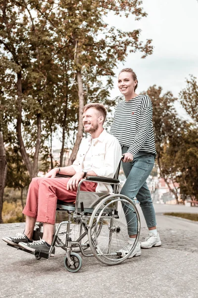 Mujer segura sonriendo y empujando la silla de ruedas de su novio discapacitado — Foto de Stock