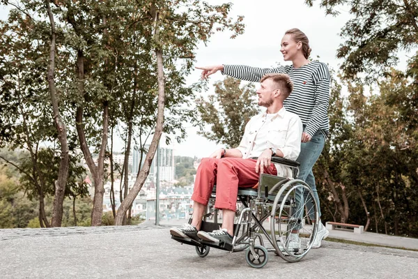 Mujer alegre sonriendo y mostrando la vista a su novio discapacitado — Foto de Stock