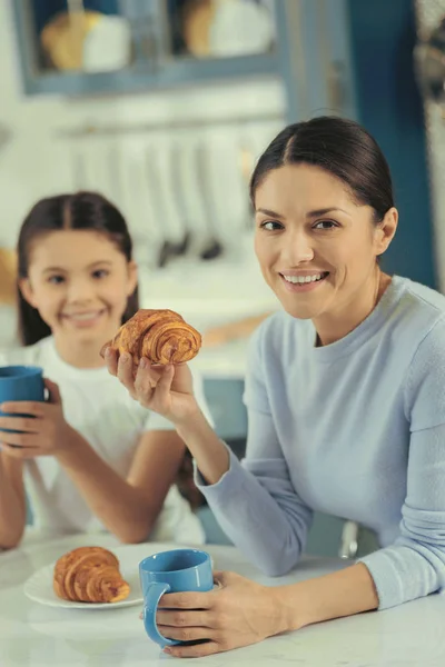Sorrindo mulher segurando croissant sentado à mesa — Fotografia de Stock