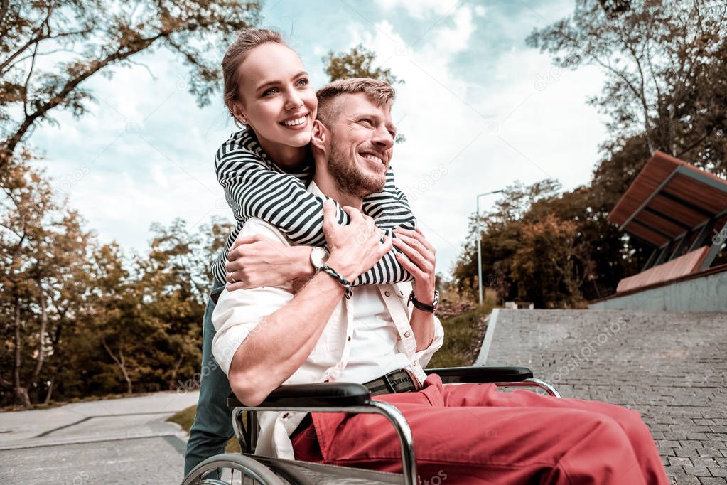 Caring woman gently hugging her disabled boyfriend and looking happy