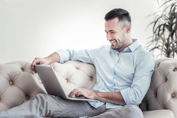 Positive delighted brunette using his laptop