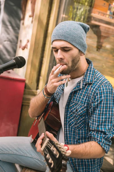 Earnest male guitarist puffing cigarette on street — Stock Photo, Image