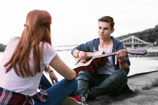 Menino bonito cantando a música para sua namorada sentada perto da ponte — Fotografia de Stock