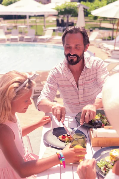 Gioioso uomo positivo che aiuta sua figlia con il cibo — Foto Stock