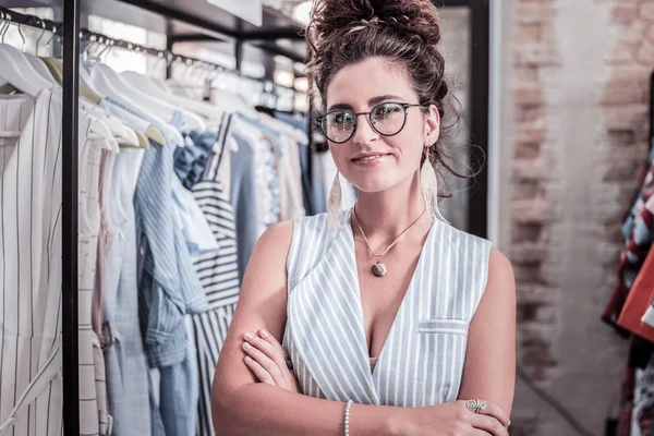 Stylish dark-haired designer wearing glasses and earrings working in her showroom