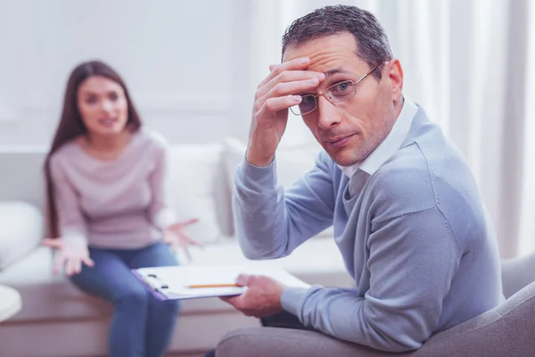 Emocionado psicólogo levemente cansado mirando hacia otro lado de su cliente — Foto de Stock