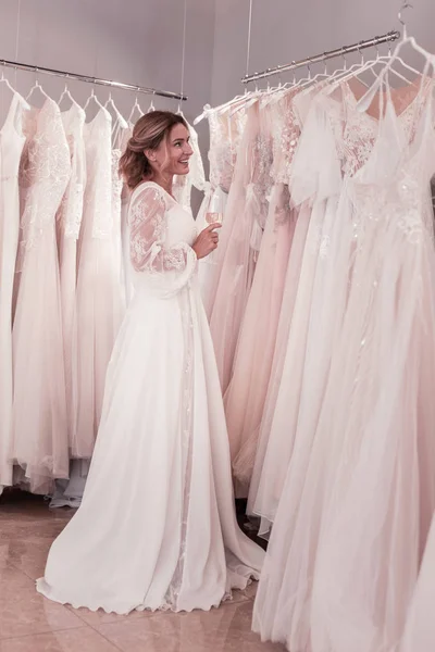 Joyful beautiful woman standing near wedding dresses