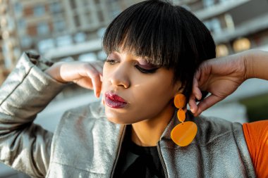 Dark-haired appealing girl showing her orange plastic earrings clipart