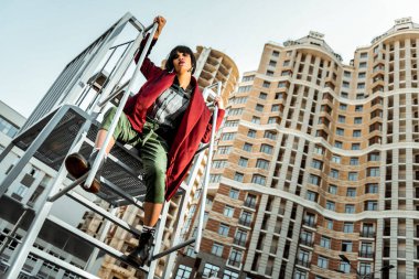 Dikkatsizce soyut kıyafetlerle metal üzerinde oturan yorgun mağrur kadın