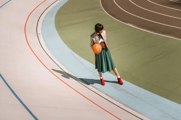ผู้หญิงผอมสูงยืนกับลูกบอลสีส้มบนสนามกีฬา — ภาพถ่ายสต็อก