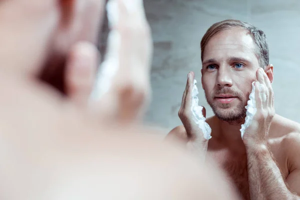 Bonito homem de olhos azuis usando espuma de barbear ao raspar o rosto — Fotografia de Stock