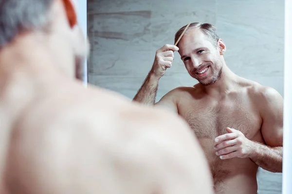 Homem barbudo e bonito penteando seu cabelo e olhando no espelho — Fotografia de Stock