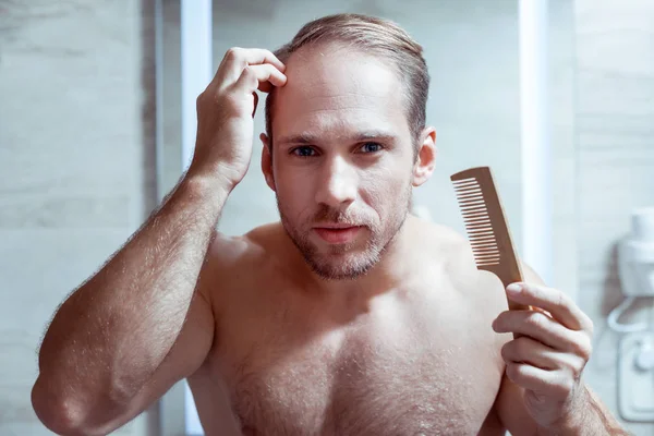 Голубоглазый мужчина расчесывает свои мокрые волосы после мытья в душе — стоковое фото
