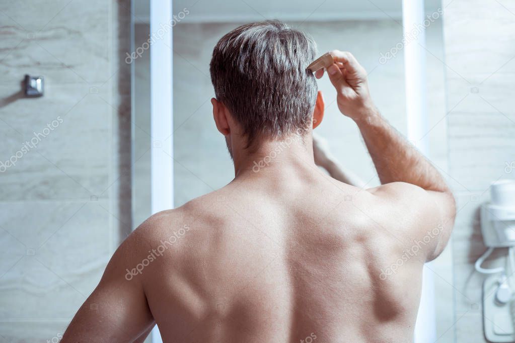 Blonde-haired man with muscle body standing in front of mirror