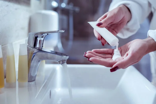 Frau gießt etwas Creme auf ihre Hände, während sie die Haut mit Feuchtigkeit versorgt — Stockfoto
