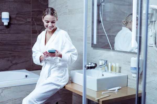 Donna dai capelli biondi che legge il messaggio sul telefono in piedi in bagno — Foto Stock
